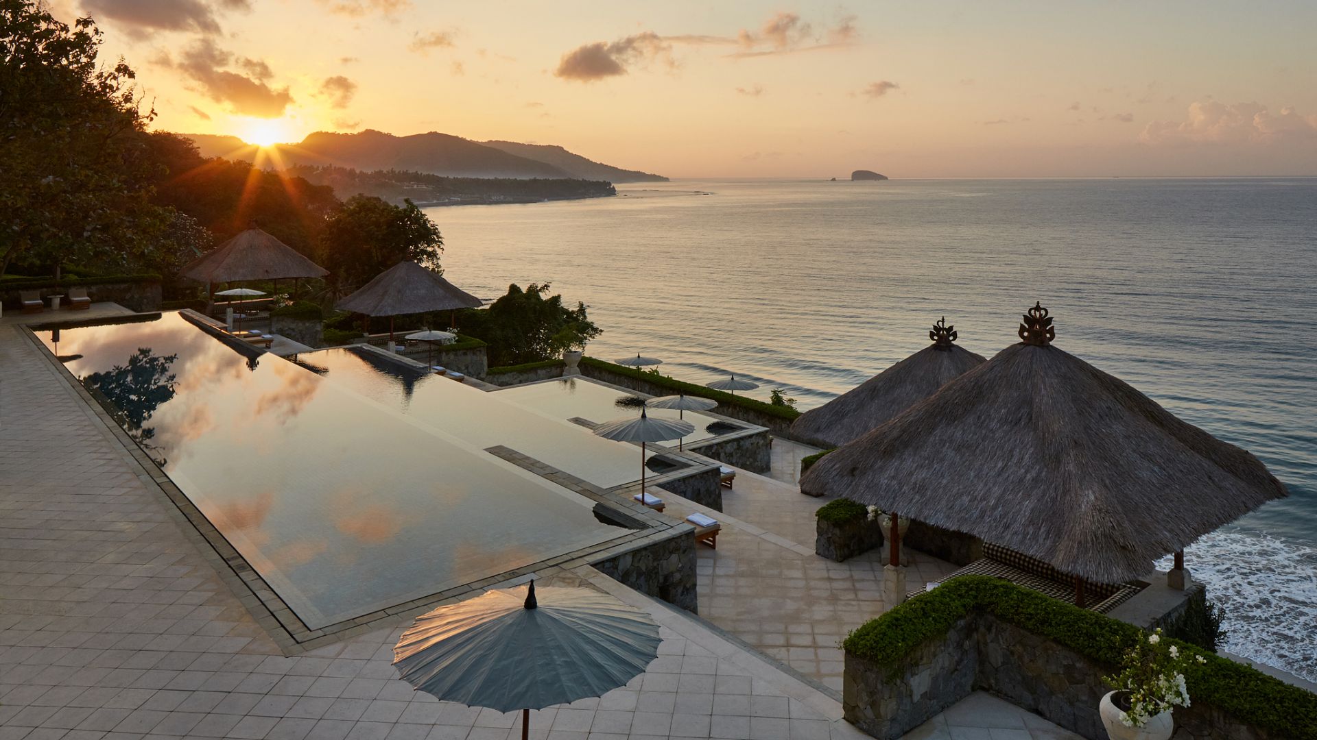 Amankila's three-tiered clifftop infinity pool and thatched bale pavilions at sunrise above the Lombok Strait in east Bali