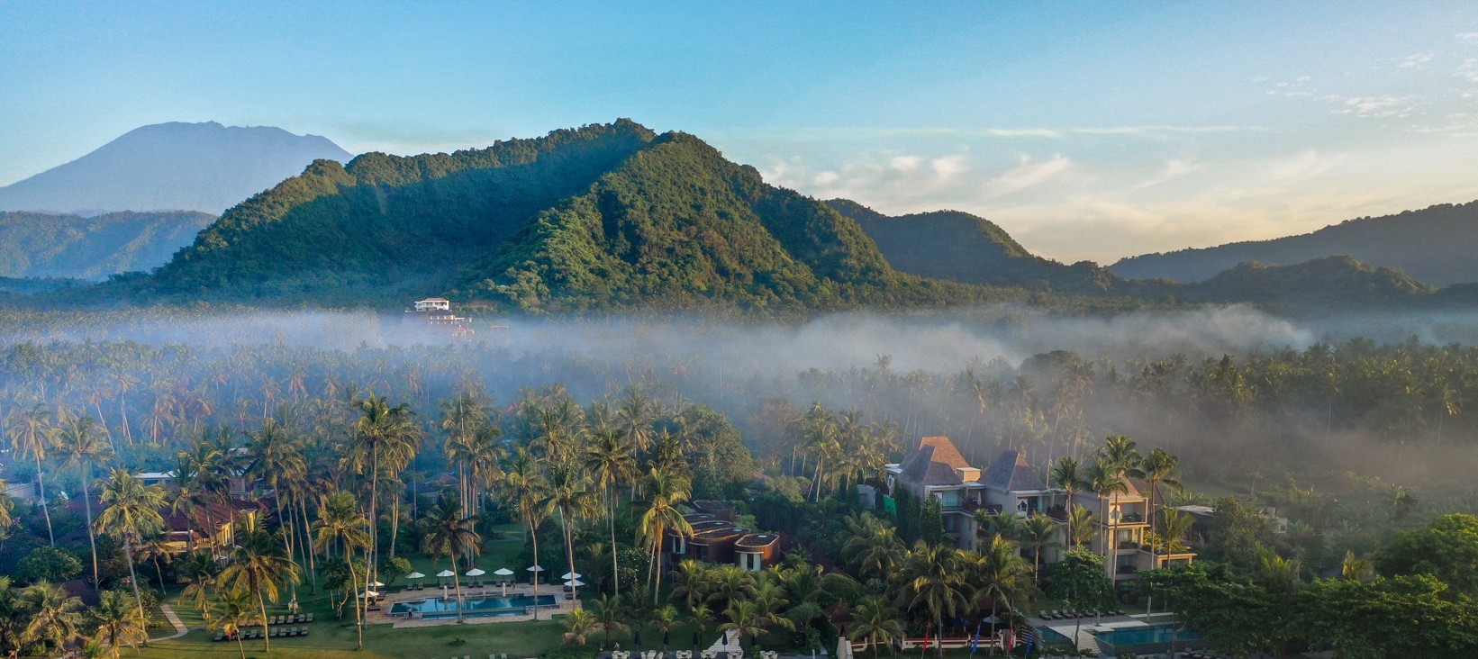 Aerial view of Candi Beach Resort & Spa nestled in a coconut-grove garden on Mendira Beach, east Bali, with mountains beyond