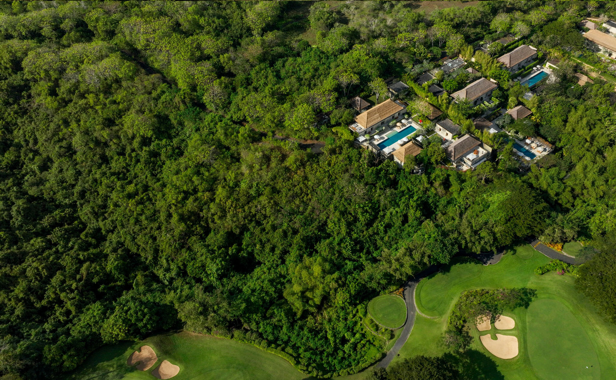 Aerial view of Aman Villas at Nusa Dua nestled in tropical forest, with private pool villas and gardens visible between dense green canopy