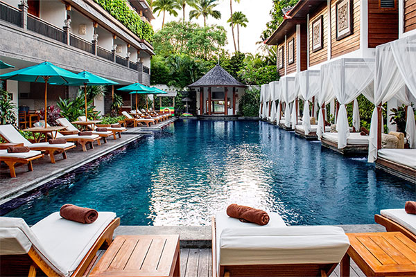 Pool lined with cabanas and loungers between resort buildings at Astagina Resort Villa & Spa, Legian