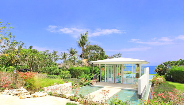 The glass Astina Chapel at AYANA Resort Bali, set in a garden with a reflecting pool and the Indian Ocean behind it