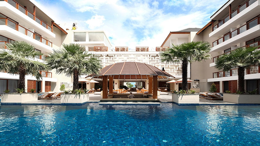 Central pool framed by palms and resort wings with a glimpse of the sea at Bali Niksoma Boutique Beach Resort, Legian
