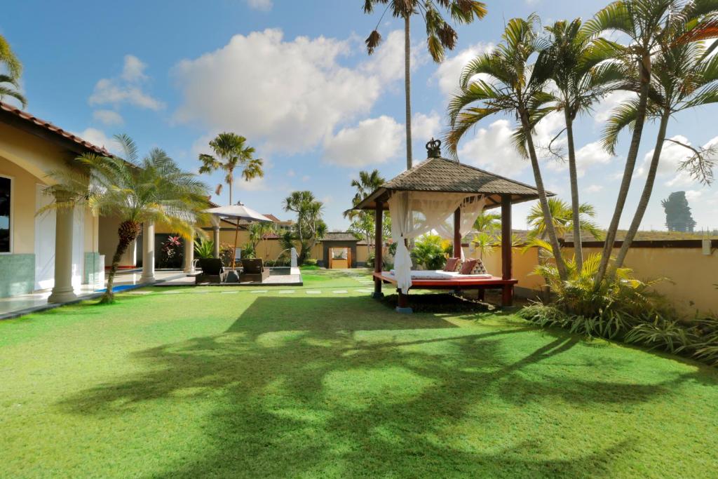 Garden lawn at The Beverly Hills Bali in Ungasan with a canopied daybed, tall palms, and the Garuda Wisnu Kencana statue in the distance