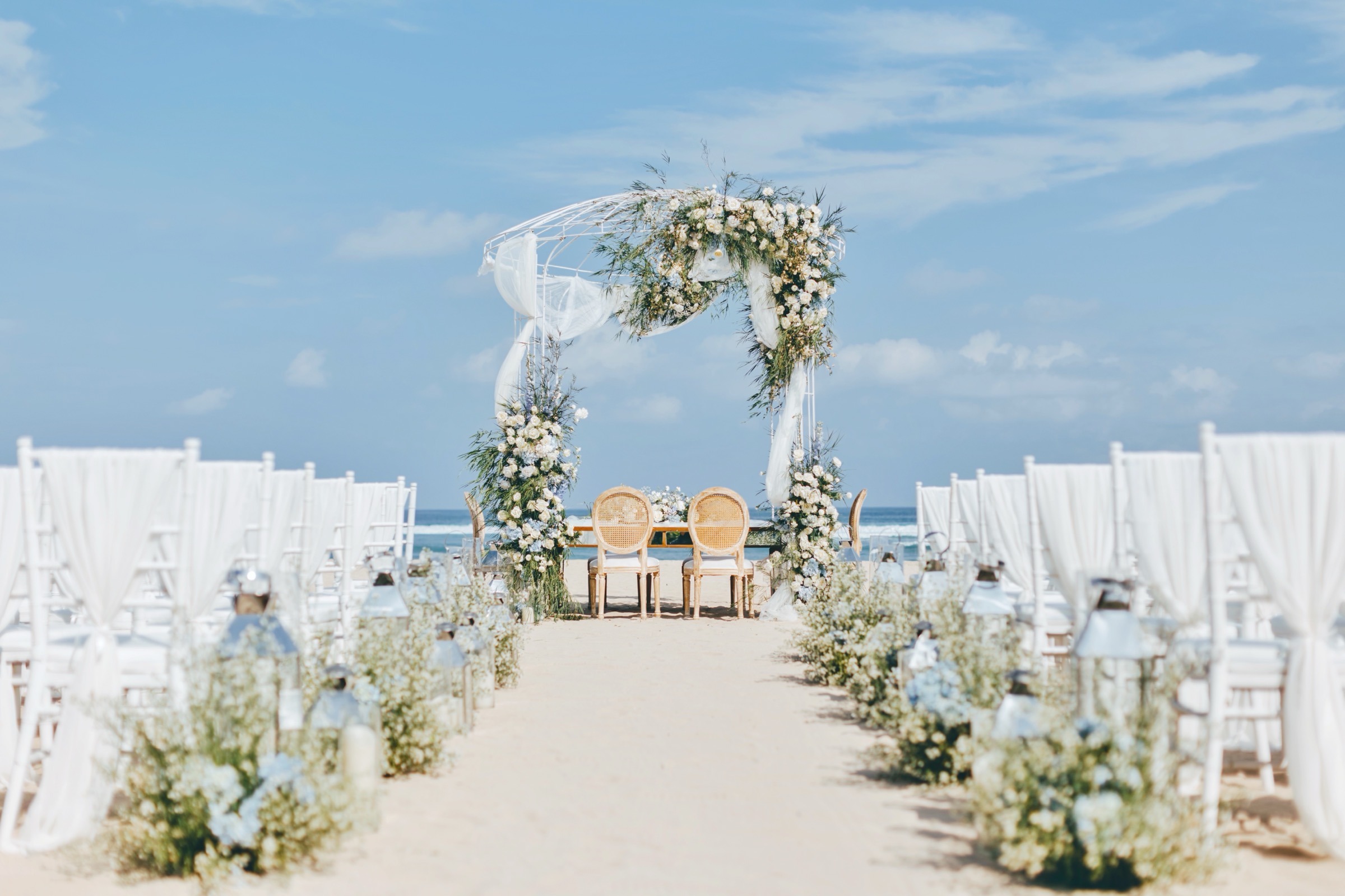 A beach ceremony set with a floral arch and white chairs facing the ocean at Grand Hyatt Bali, Nusa Dua