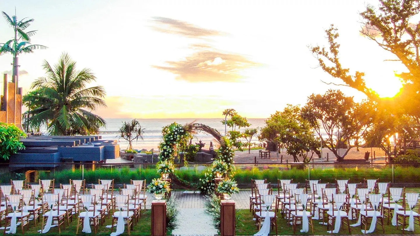 Beachfront ceremony setup at sunset at Hotel Indigo Bali Seminyak Beach, with ocean view and floral arch