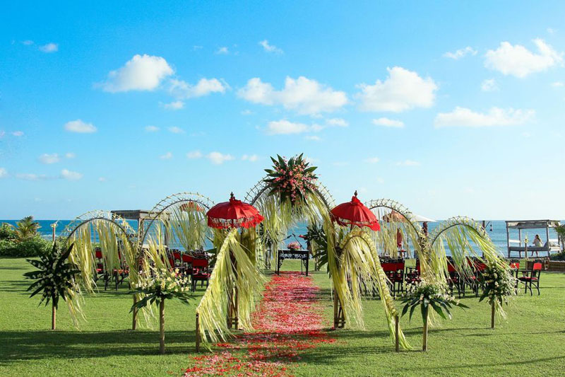 Beachfront lawn set for a wedding with palm-leaf arches and ocean behind at Hotel Tugu Bali, Canggu