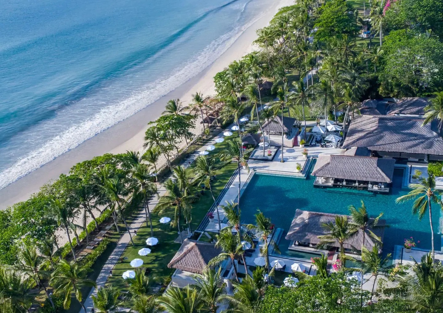 Aerial view of InterContinental Bali Resort's beachfront pools, thatched pavilions, and palm gardens along Jimbaran Bay