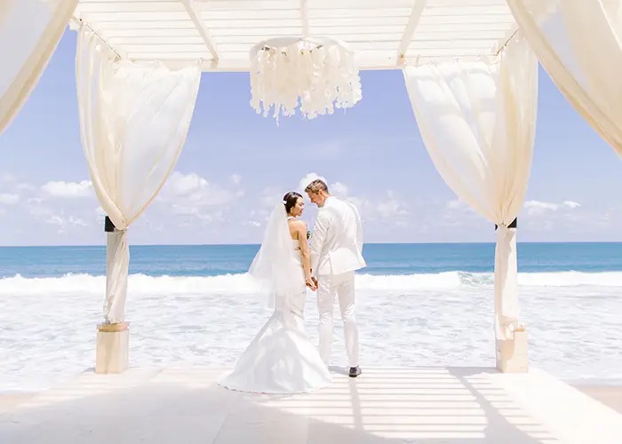 A couple beneath a beachfront pavilion at The Seminyak Beach Resort & Spa, the Indian Ocean framed behind them