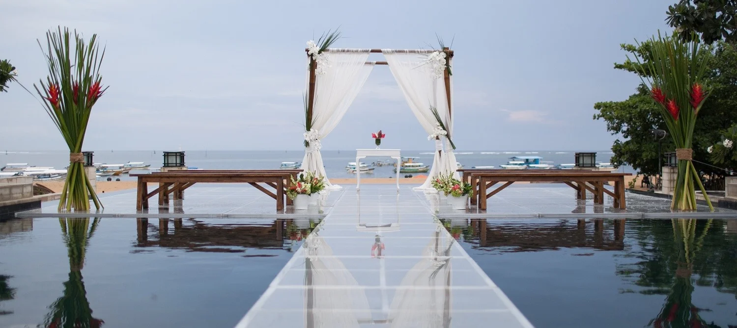 Wedding arch on the glass aisle over the pools at The Sakala Resort Bali, with Tanjung Benoa Beach behind