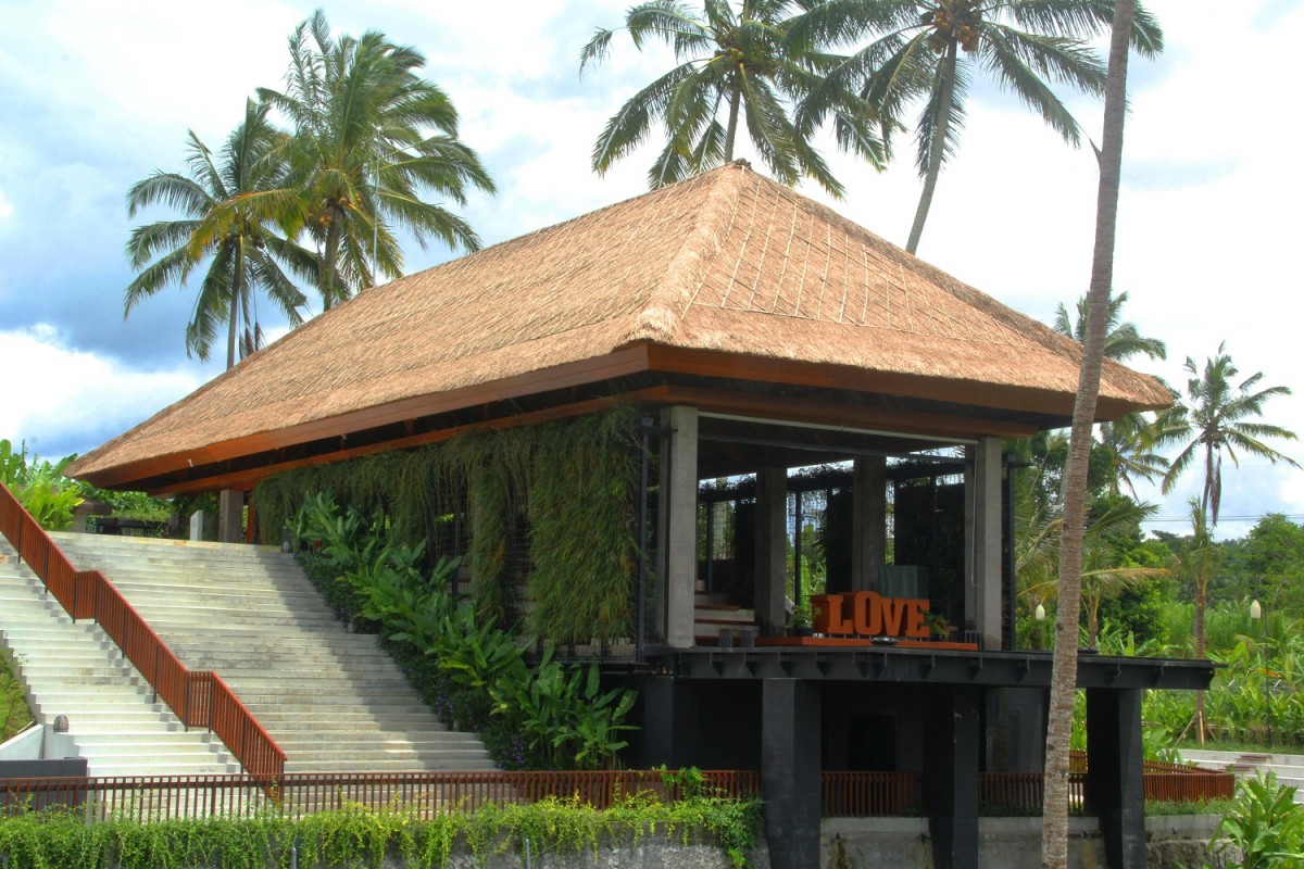 The Secret Chamber chapel at Secret Garden Village, a thatched-roof pavilion on stilts beside an amphitheatre staircase, framed by palms and jungle in the Bedugul highlands