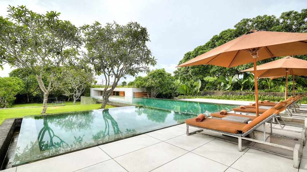 The Iman Villa's 21-metre infinity pool overlooking terraced rice fields in Pererenan, Canggu, with frangipani trees and open-air pavilion