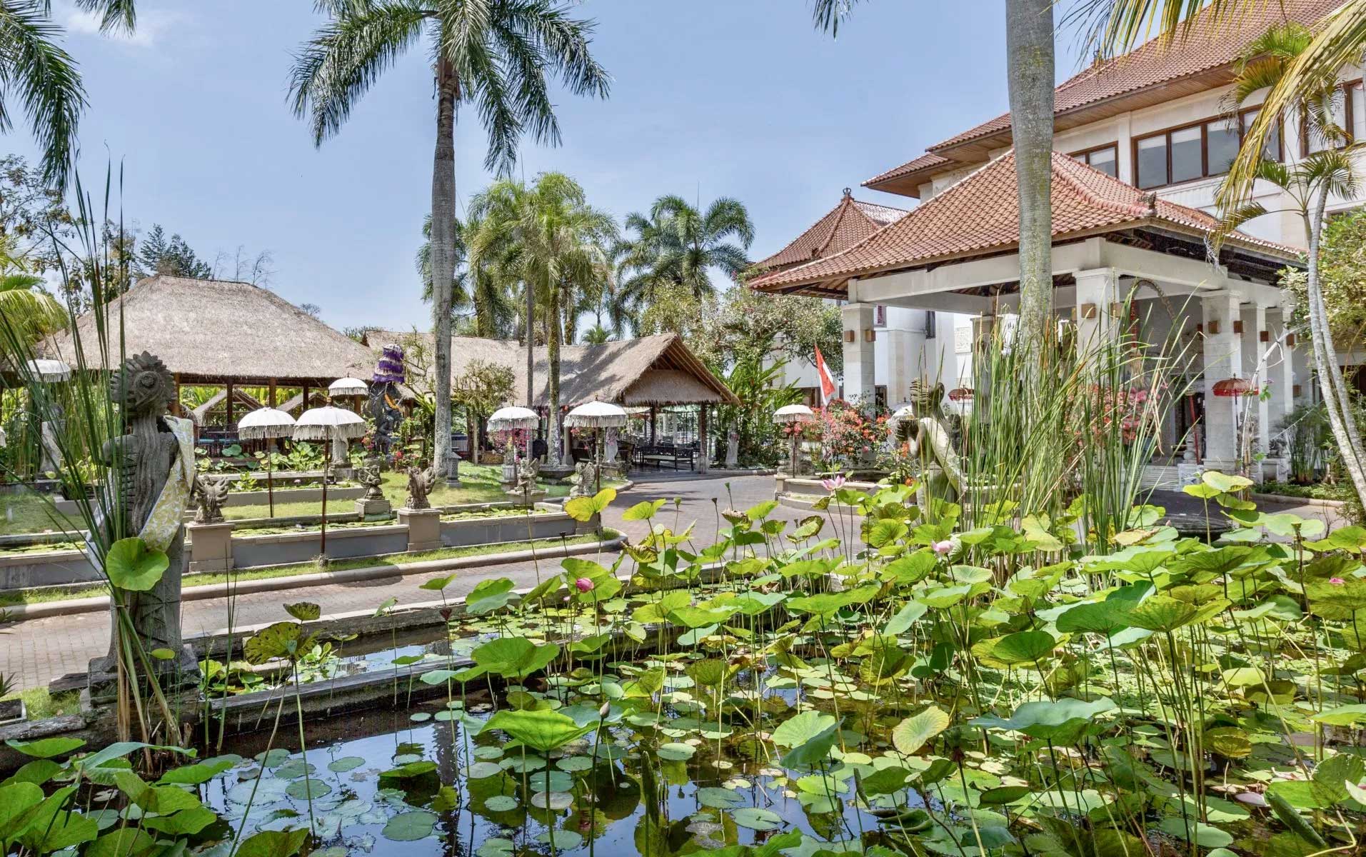 Lotus ponds, carved statues, and thatched pavilions in the gardens of The Mansion Resort in Ubud