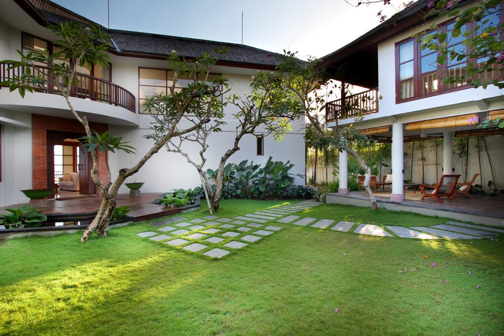 Manicured garden courtyard at Villa Ali Agung with frangipani trees, a lily pond, and stepping-stone lawn