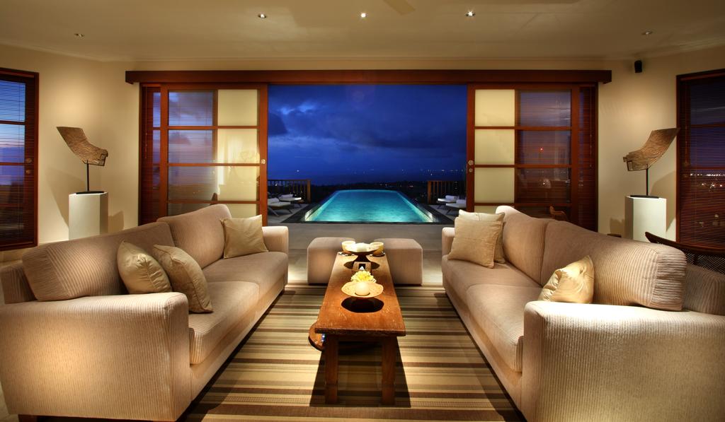 Living room at Villa Ali Agung at dusk, framing the infinity pool and lights of the coast below