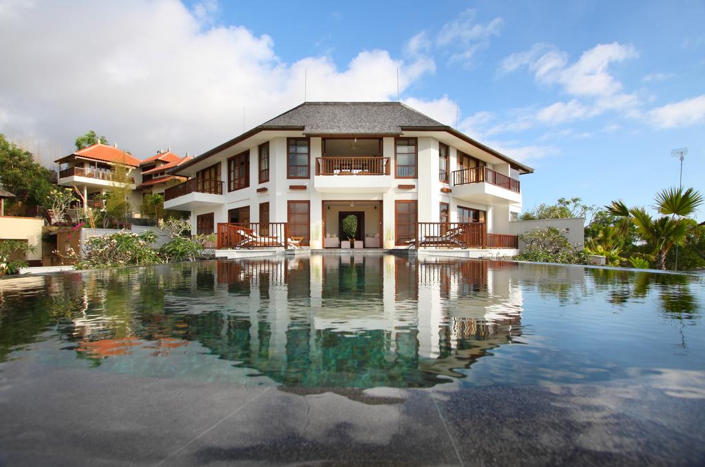 The two-storey Balinese villa at Villa Ali Agung reflected in its infinity pool under a blue sky