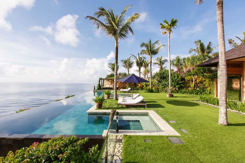 Cliff-edge infinity pool and lawn at Villa Ambar, The Ungasan, with palms and the Indian Ocean stretching to the horizon