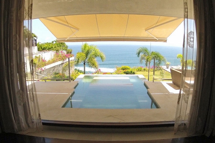 Villa Anugrah's shaded pool cabana framed by palms, ocean beyond