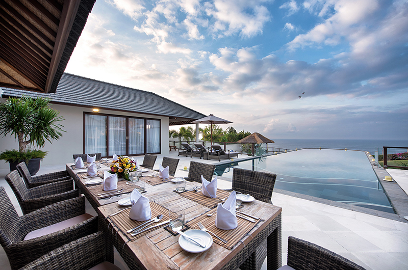 The clifftop dining terrace and infinity pool at Villa Bale Agung in Ungasan, table set for guests with the Indian Ocean beyond the pool edge