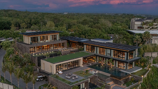 Aerial dusk view of Villa Bie, a multi-level modern villa lit up among the trees of the Six Senses Residences hilltop in Pecatu, Uluwatu