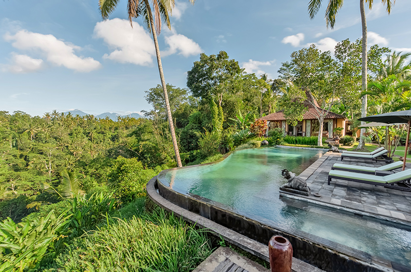 Villa Bodhi's lagoon-style infinity pool at the edge of the jungle valley near Ubud, with distant mountains and sun loungers