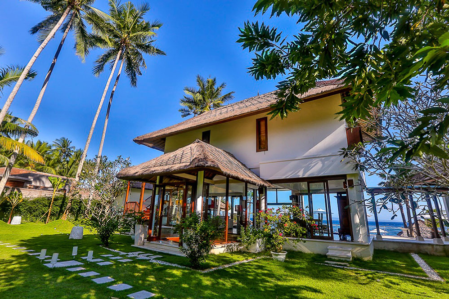 Villa Jukung's colonial-style exterior among palm trees, with the East Bali coastline behind