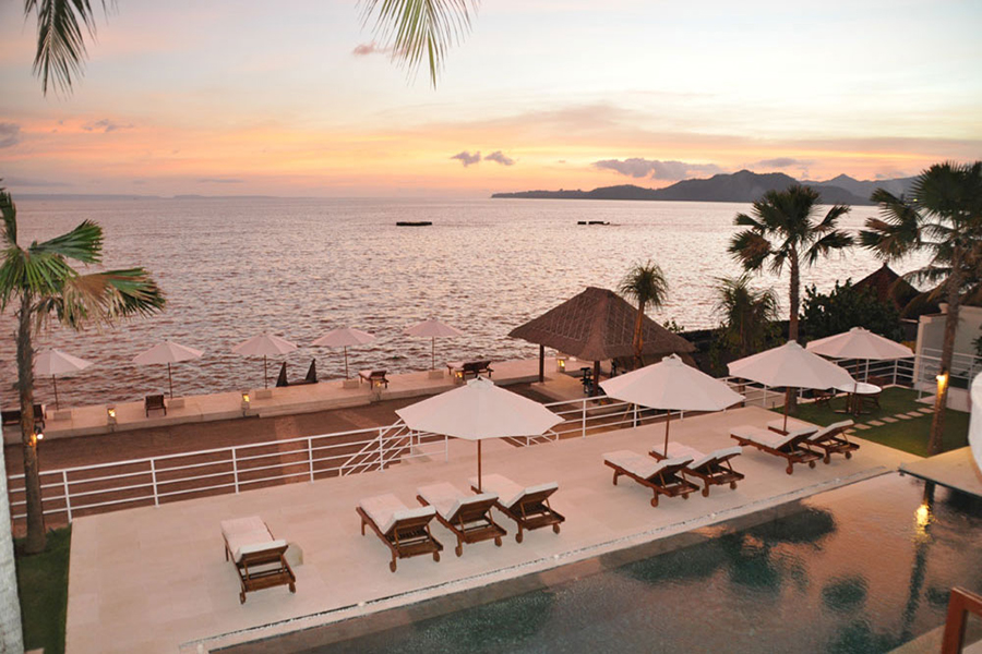 Sunset over the sea from Villa Jukung's outdoor deck, with loungers and umbrellas along the shore