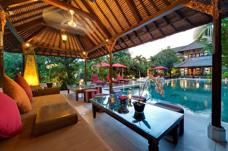 Villa Kalimaya's pool and garden at dusk, seen from an open pavilion with red umbrellas, Laksmana Seminyak