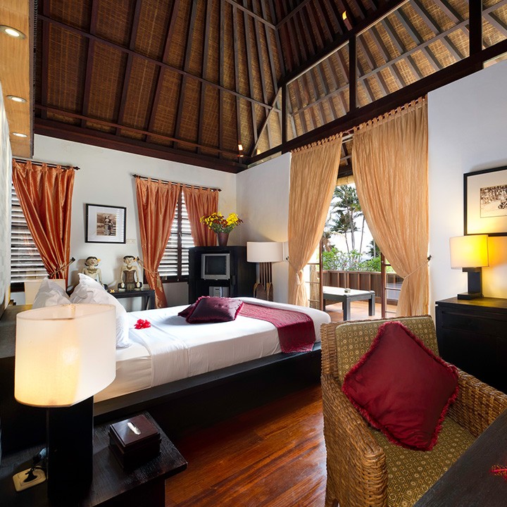 Bedroom under a high timber Joglo roof with a garden terrace at Majapahit Beach Villas
