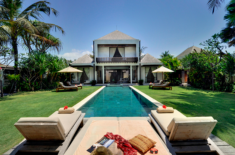 Two-storey villa and long pool framed by palms and lawn at Majapahit Beach Villas, Ketewel