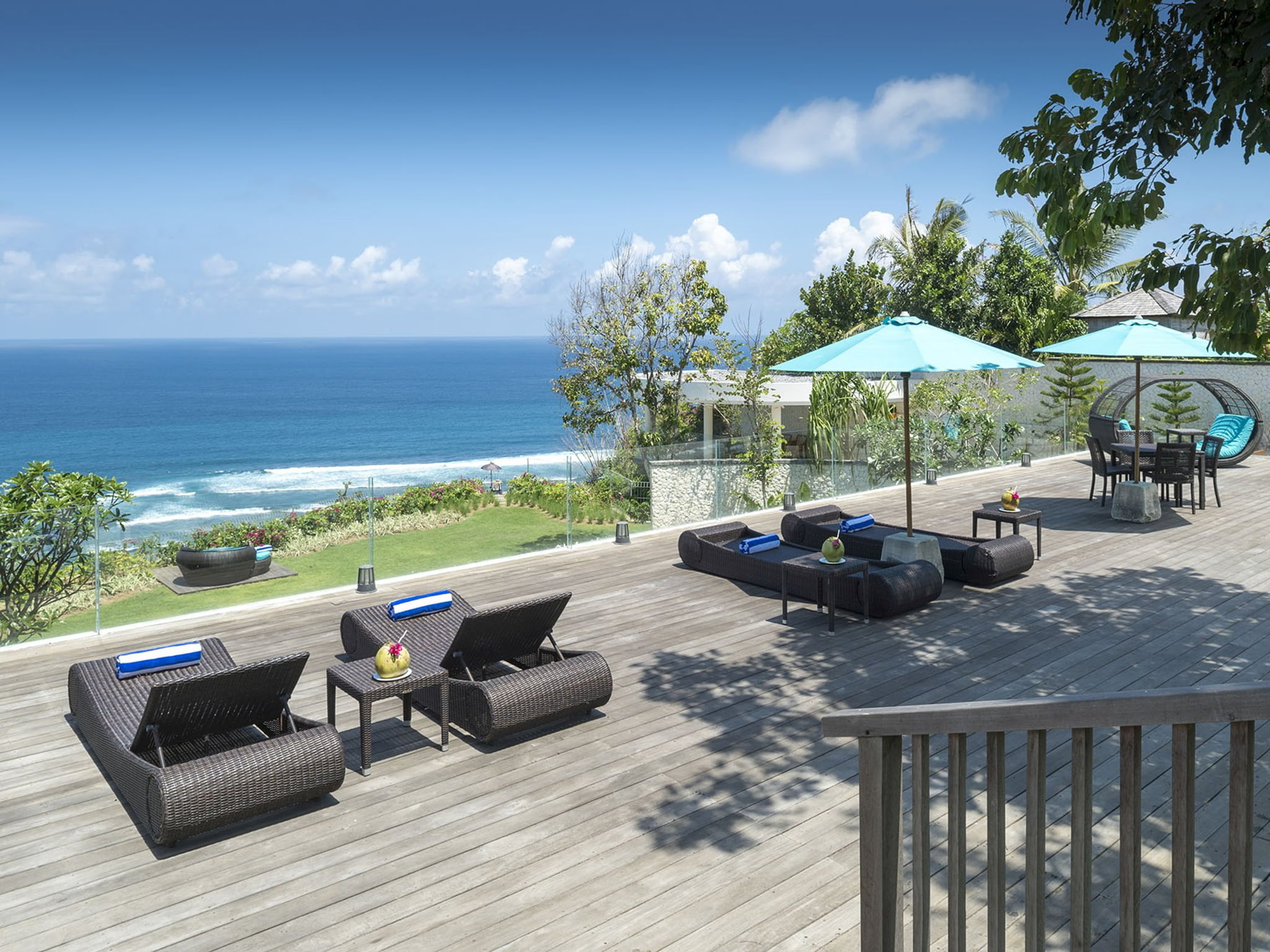 Ocean-view timber deck with loungers and parasols at Villa Markisa, Pandawa Cliff Estate, the Indian Ocean and surf beyond