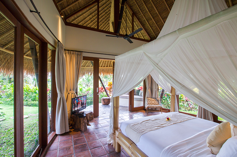 Canopy bed in a thatched-roof bedroom pavilion at Villa Omah Padi, opening onto the garden