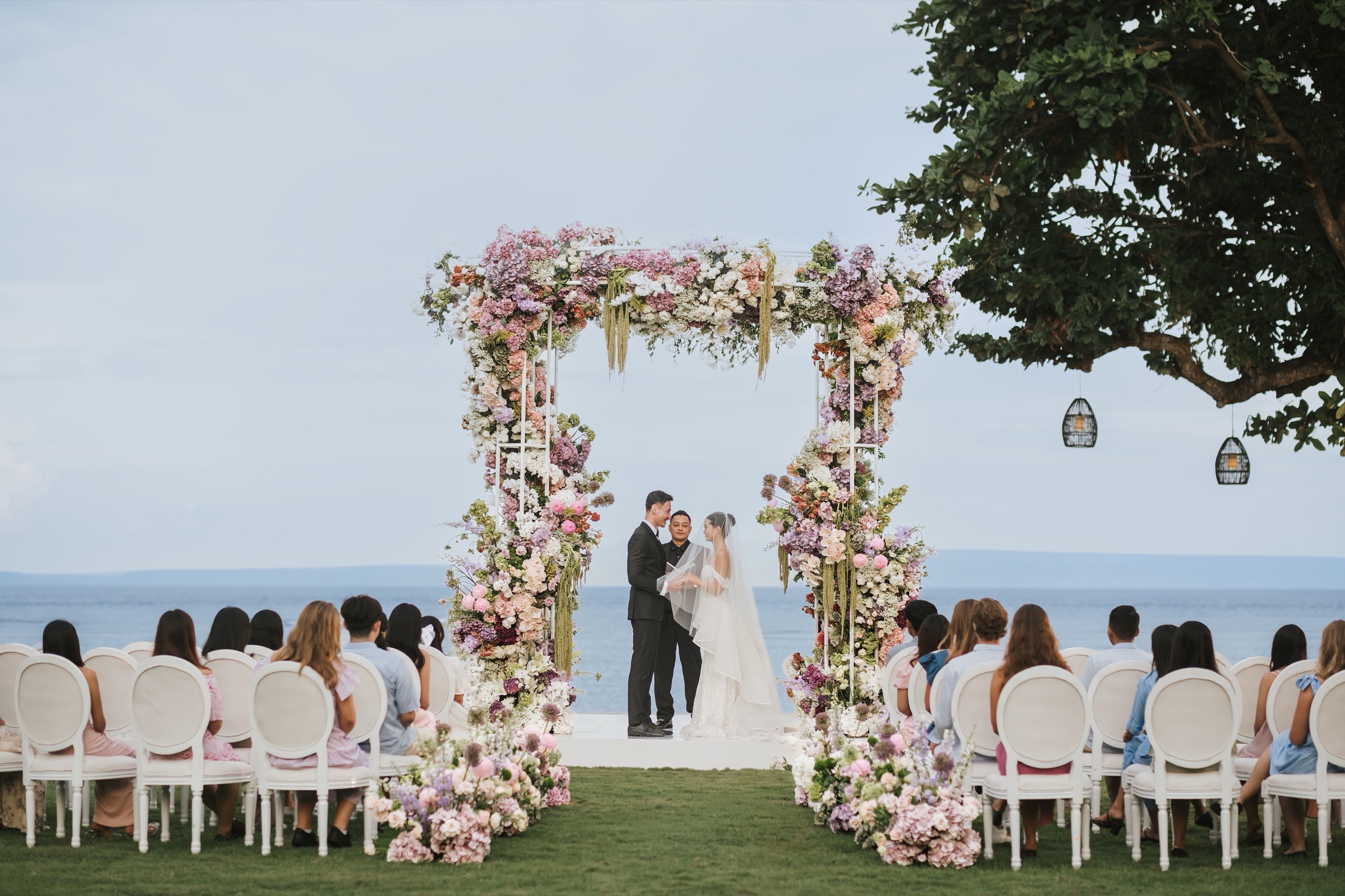A garden ceremony set with a floral arch and white chairs facing the ocean at The Westin Resort Nusa Dua, Bali